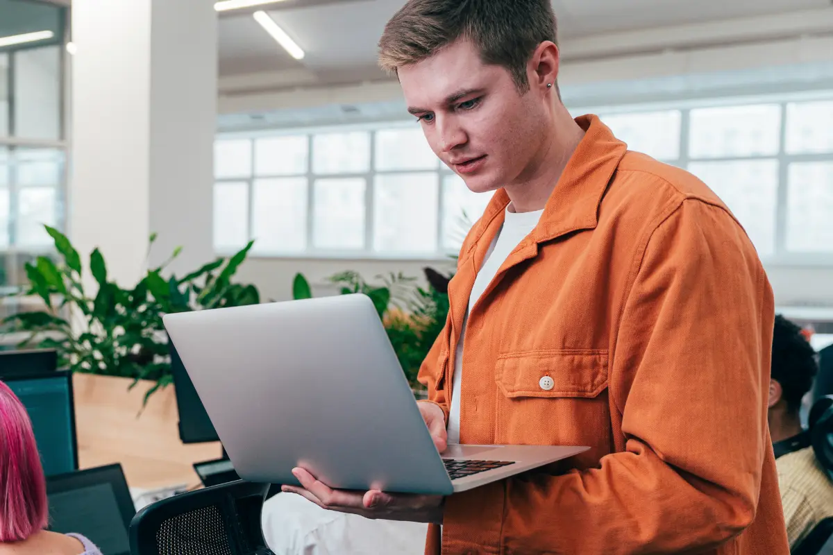 Man wearing orange jacket in office looking concerned at laptop