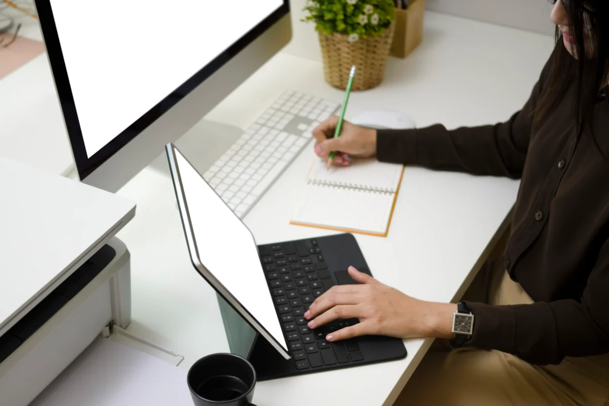 Businesswoman searching information on computer tablet and making note on notebook at office